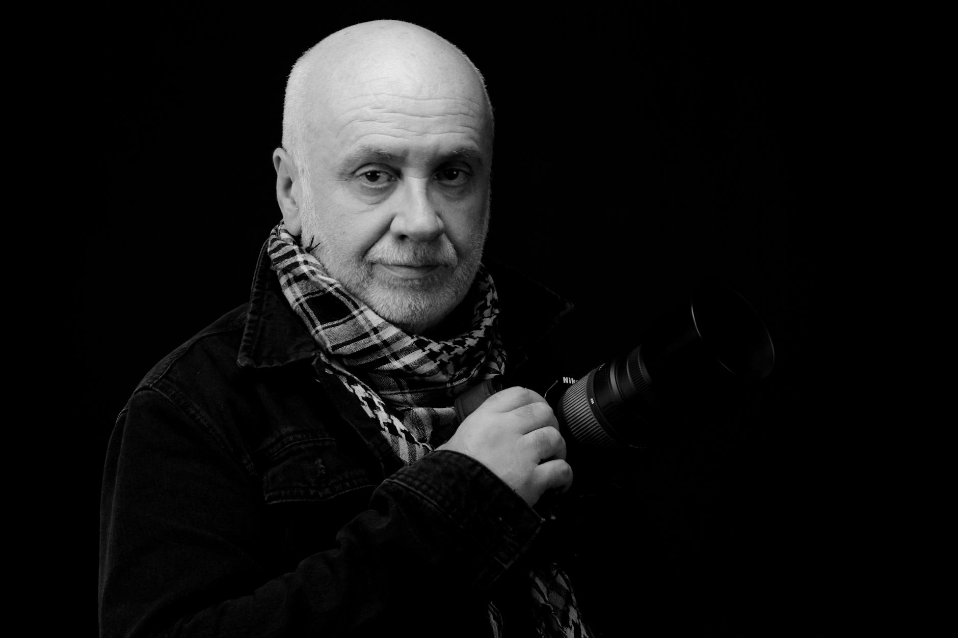 Striking black and white portrait of an elderly photographer holding a camera.